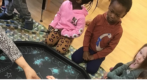 preschool children gathered around a tuff tray with coloured cornstarch and patterns 