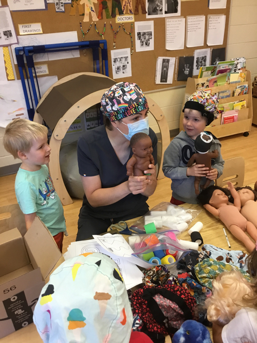 doctor talking to children while holding a doll and sitting at a table