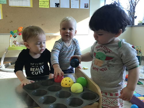 infants playing with balls in a muffin tin