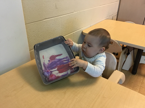 infant playing with a painting inside a box
