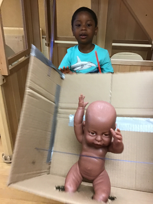 boy pushing a baby doll in a homemade baby swing made of cardboard