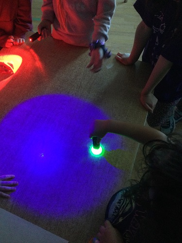 Children shining coloured light on a table top