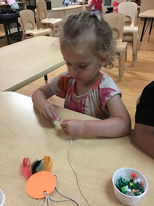 Preschool girl sitting at table adding beads to her dream catcher