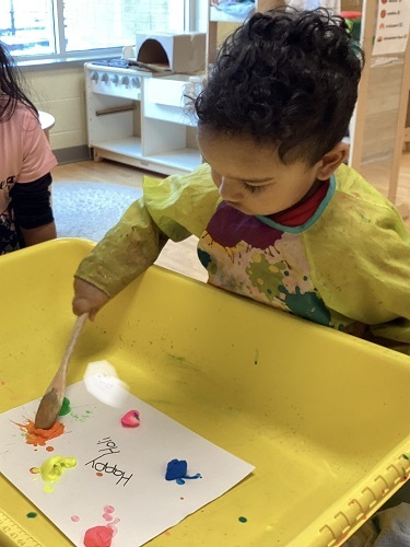 A child using a wooden spoon to create colour splats on paper