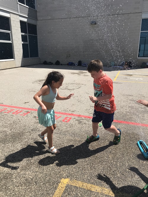 2 school aged children jumpimg in water puddle
